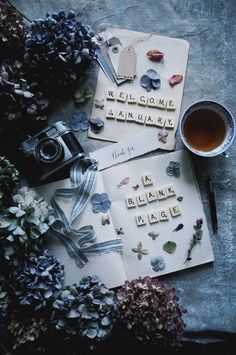 an assortment of flowers and letters on top of a table next to a cup of tea