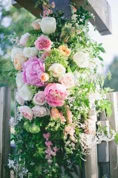 a bunch of flowers that are hanging from a wooden structure with greenery on it