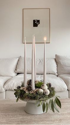 three candles are placed in a white bowl with greenery and flowers on the table