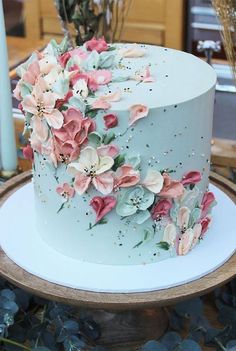 there is a blue cake with pink flowers on the top and white frosting around it