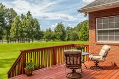 a wooden deck with two rocking chairs and a table on it, in front of a red brick house