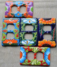 four colorful flowered switchplates sitting on top of a cloth covered table next to each other