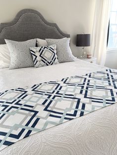 a bed with white and blue pillows on top of it next to a window in a bedroom