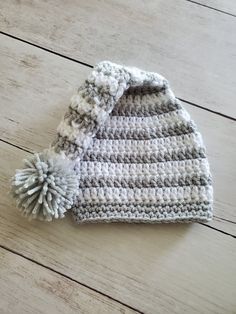 a crocheted hat with a pom - pom on the side sitting on a wooden floor