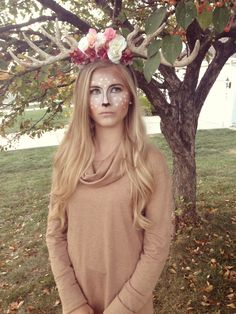 a woman standing under a tree with her face painted like a flower crown on her head