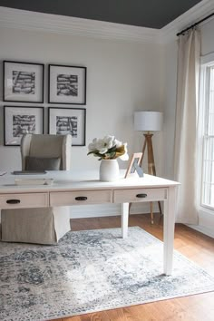 a white desk with flowers on it in front of some framed pictures and a lamp