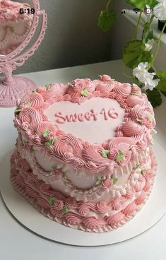 a pink heart shaped cake sitting on top of a white table next to a vase with flowers