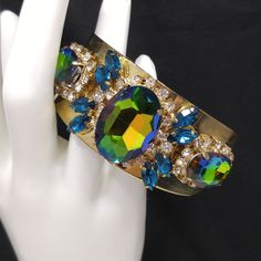 *Description: This is a gorgeous watermelon rhinestone crystal bracelet on a golden brass cuff which glitters and sparkles in the light. The vintage rhinestones are secured on a golden brass cuff and the reflective cuff adds additional sparkle to the bracelet. There is one large watermelon rhinestone in the center, surrounded by clear rhinestones and sapphire blue marquise cut rhinestones. On each side of the center stone are two more watermelon rhinestones, a little smaller in size, one on each Crystal Bangle Cuff Bracelet For Party, Crystal Bracelet With Jewels For Parties, Crystal Bracelets With Jewels For Parties, Party Crystal Bracelets With Jewels, Metal Crystal Bracelet With Sparkling Stones For Party, Adjustable Jeweled Crystal Bracelet For Parties, Adjustable Crystal Bracelet With Jewels For Party, Gold Jeweled Cuff Bracelet For Party, Glamorous Crystal Cuff Bracelet For Party