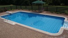 an above ground swimming pool surrounded by brick pavers and fenced in lawn area