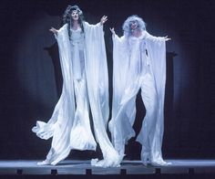 two women dressed in white on stage with one holding her arms out to the side