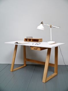 a desk with a lamp on top of it next to a white wall and wooden floor