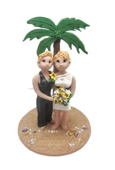 a wedding cake topper with a bride and groom under a palm tree on the beach