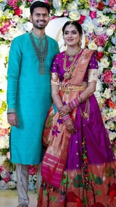 a man and woman standing next to each other in front of a floral wall with flowers