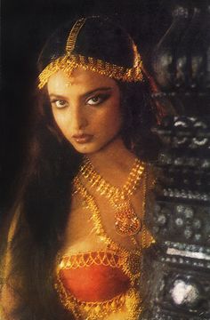 a woman with long black hair and gold jewelry on her head is looking at the camera