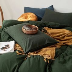 a bed with green sheets, pillows and a bowl on top of the comforter