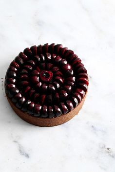 a chocolate cake on a marble surface with red beads around the edges and a cherry center