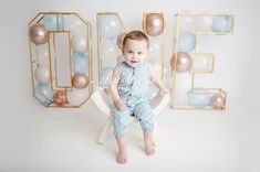 a baby boy sitting on a chair in front of balloons