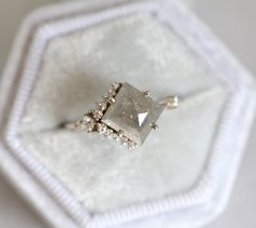 a diamond ring sitting on top of a white cloth covered box with beading around it