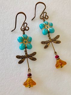 "Adorable turquoise blue Czech glass puffed daisies with topaz yellow bellflowers and vintage bronze stamped dragonfly charms. Matte turquoise 14 mm Czech glass puffy 5 petal flowers are etched with metallic gold and wire wrapped in vintage bronze with 6 x 9 mm translucent topaz yellow bellflowers accented with tiny burnt orange crystals. Lightweight dangles hang on handmade and hammered vintage bronze ear wires. Total drop length is 2 1/2\"." Whimsical Blue Flower Earrings For Gift, Blue Whimsical Dangle Flower Earrings, Vintage Turquoise Flower Earrings, Whimsical Blue Dangle Flower Earrings, Nickel-free Czech Glass Flower Earrings, Handmade Blue Whimsical Flower Earrings, Whimsical Handmade Blue Flower Earrings, Unique Blue Flower Earrings With Ear Wire, Turquoise Flower-shaped Earrings With Flower Charm