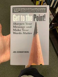 a person holding up a book about how to get to the point with a pencil sticking out of it