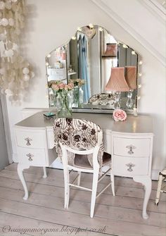 a white vanity with a mirror and flowers on it in a room next to stairs