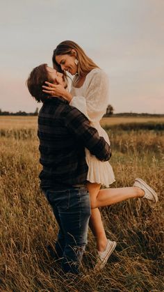 a man holding a woman in the middle of a field with tall grass on both sides