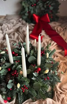 a christmas arrangement with candles and greenery on a bed next to a red ribbon