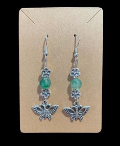 the earrings are decorated with green beads and silver butterfly charmes on top of each other