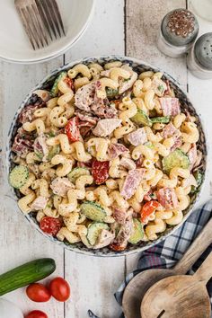 a bowl filled with pasta salad next to other ingredients and utensils on a white wooden table