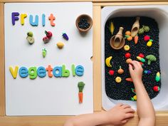 a child is playing with vegetables and fruits in a play tray that says fruit vegetable