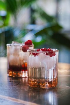 two glasses filled with ice and cranberries on top of a wooden table next to each other