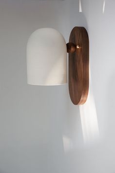 a wooden wall light with a white shade on it's side and a lamp attached to the wall