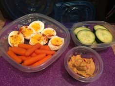 three plastic containers with eggs, carrots and cucumbers on a purple counter