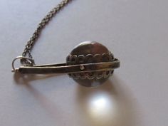 an antique silver ball and chain on a white surface with a pearl in the foreground