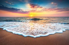 the sun is setting over the ocean with waves coming in to shore and sand on the beach