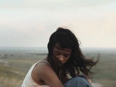 a woman sitting on the ground with her hair blowing in the wind and looking down