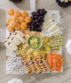 a platter with crackers, grapes, carrots, cheese sticks and other snacks