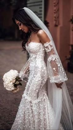 a woman in a wedding dress and veil walking down the street with flowers on her bouquet