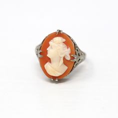 Gorgeous antique circa 1920s era Art Deco 10k white gold genuine shell cameo ring! This stunning statement ring features a genuine carved shell cameo that depicts a women in white on a peachy pink background. There are intricate filigree style details covering the setting, and the piece features the rare Ostby and Barton Maltese cross marking on the inside of the band. A beautiful piece of fine Art Deco era jewelry! *Sale - price reduced from $475 USD to $465 USD.  ERA - Circa 1920s - Art Deco  METAL / MATERIAL - 10k white gold, genuine carved shell cameo. MARKINGS / HISTORY - Inside of band is marked "OB 10K" with a Maltese cross for Ostby & Barton. Ostby (Co-owner of company) was a first class passenger on the Titanic & was among one of the 1,500 passengers who perished during the tragic Vintage Intaglio Round Rings, Vintage Round Intaglio Ring, Vintage Carved Rings For Formal Events, Vintage Carved Rings For Formal Occasions, Classic Cameo Rings, Vintage Carved Filigree Ring For Formal Occasions, Vintage White Gold Filigree Ring, Art Deco Oval Cameo Rings, Antique Carved Filigree Ring For Formal Occasions