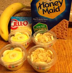 four plastic cups filled with yogurt and bananas next to a package of honey maid