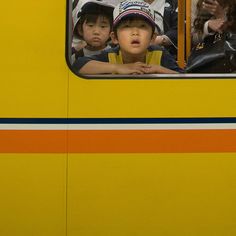 two young boys are looking out the window of a yellow bus as others look on