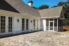 a white house with black roof and brick walkway leading up to the front door area