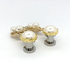 two gold and white pearls are attached to the handles of some jewelry pieces on a white surface