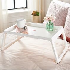 a white tray with a cup on top of it sitting on a bed next to pillows