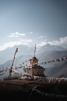 there are many flags flying in the wind on this mountain side house with mountains in the background