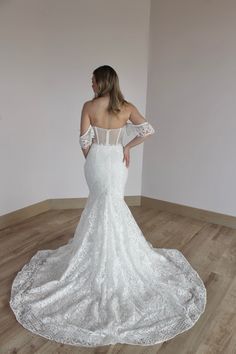 a woman in a white wedding dress standing on a wooden floor looking at the wall