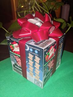 a box with a red bow on it sitting on a green tablecloth next to a potted plant