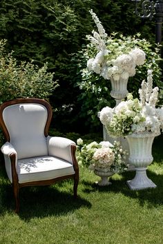 two white vases filled with flowers next to a chair