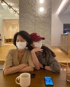 two people sitting at a table with masks on their faces, one woman is holding the other