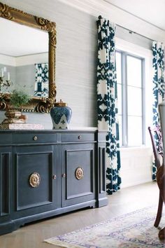 a dining room with blue and white curtains, an ornate mirror, and a wooden sideboard